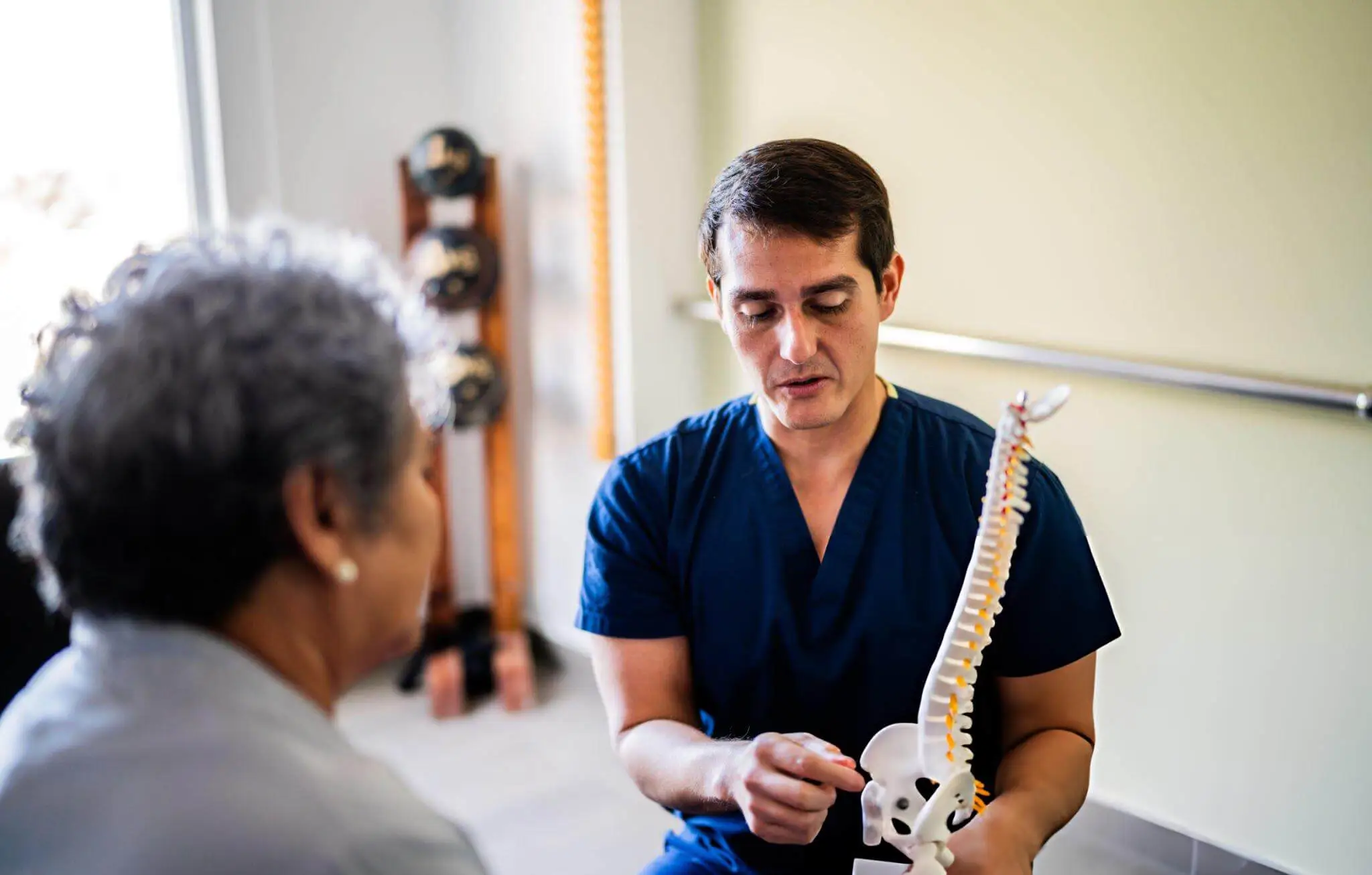 Medical professional explaining spinal health using a spine model in a rehabilitation clinic, symbolizing global issues related to spinal cord injuries.