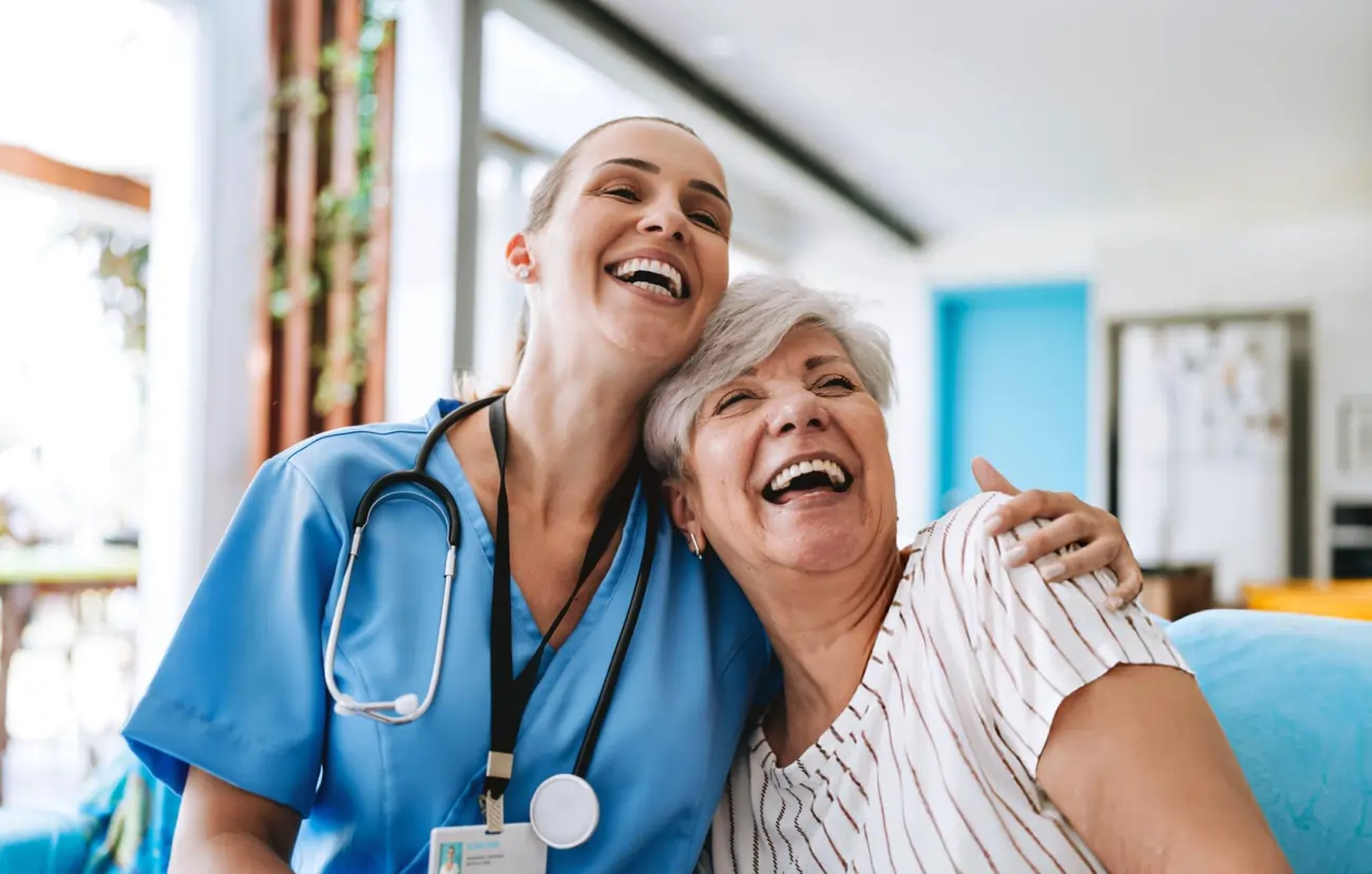 A compassionate nurse and a happy elderly woman smiling and embracing, showcasing the positive patient experience with stem cell therapy in Newport News, VA.