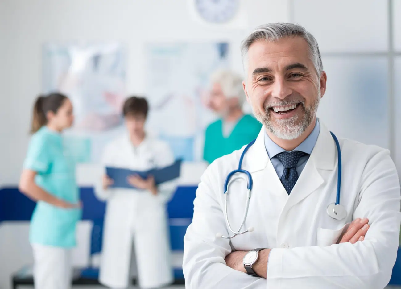 Smiling, confident doctor with arms crossed in a clinic or hospital setting.