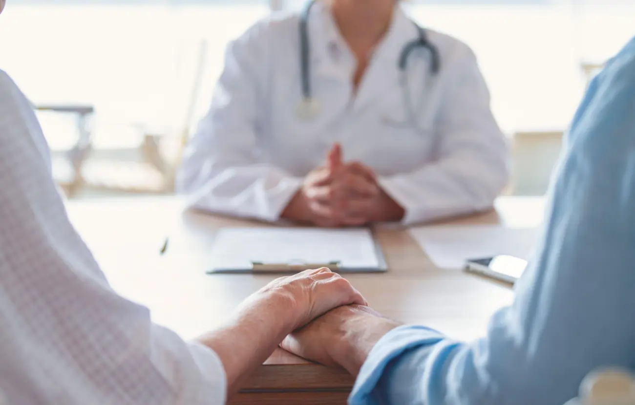 Doctor consulting with an older couple, holding hands in a show of support.