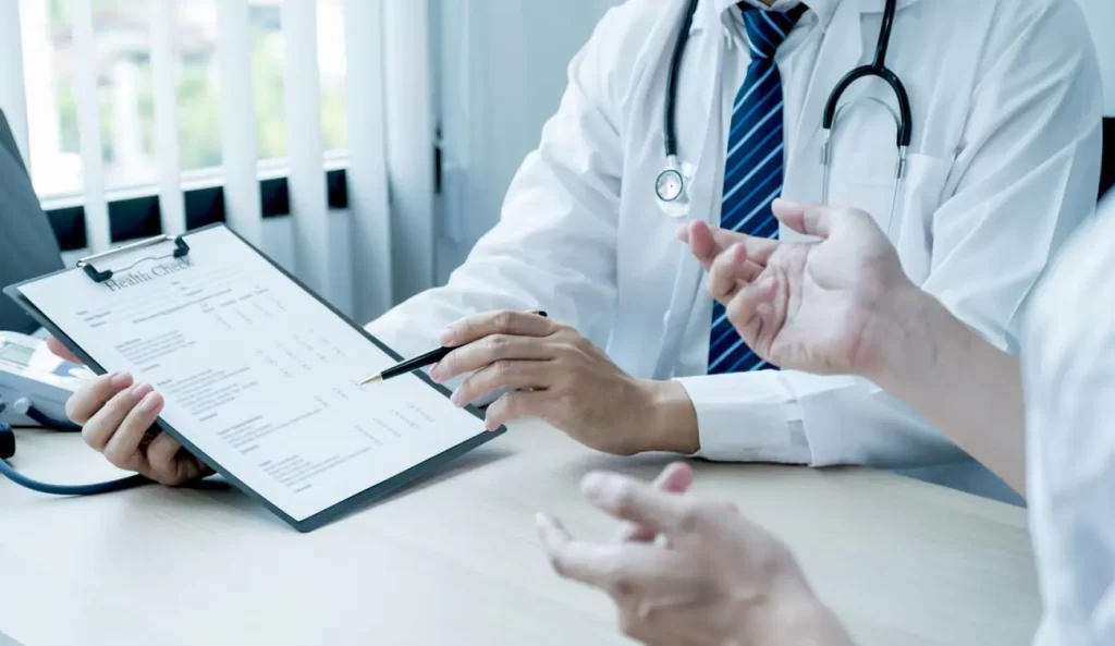 A doctor with a stethoscope discusses a health check form with a patient, representing a professional and caring medical consultation experience for those considering treatments like stem cell therapy.