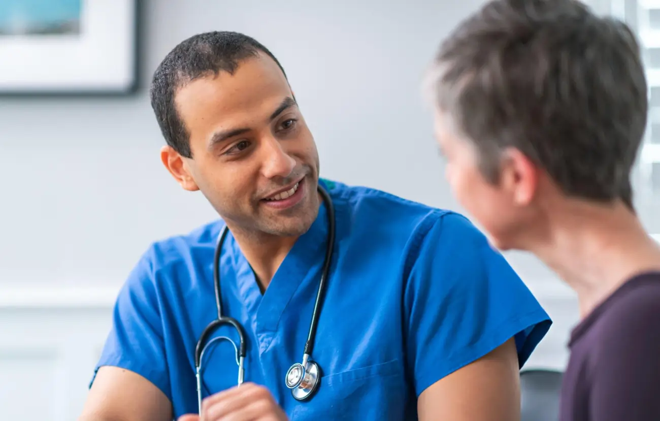 Caring doctor in blue scrubs and stethoscope talking with an older patient.