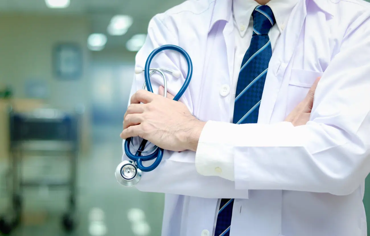 A professional doctor with a stethoscope and folded arms, in a clinic.