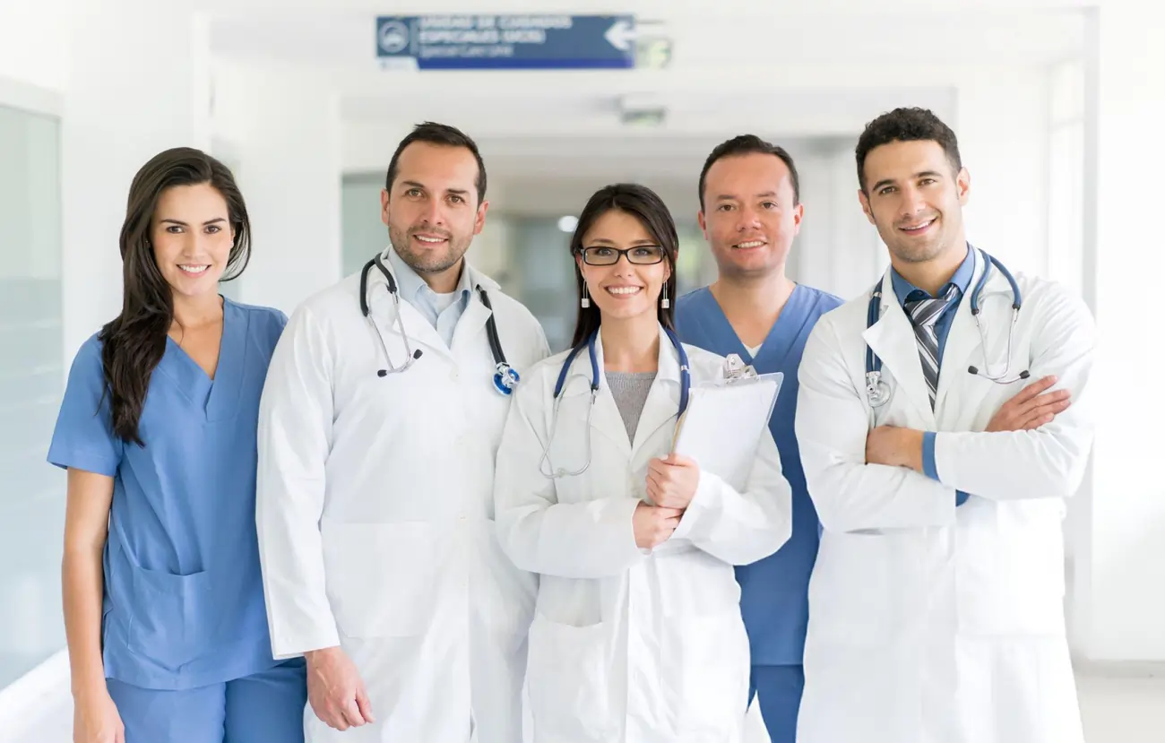 Group of professional doctors and medical staff smiling in a hospital hallway.