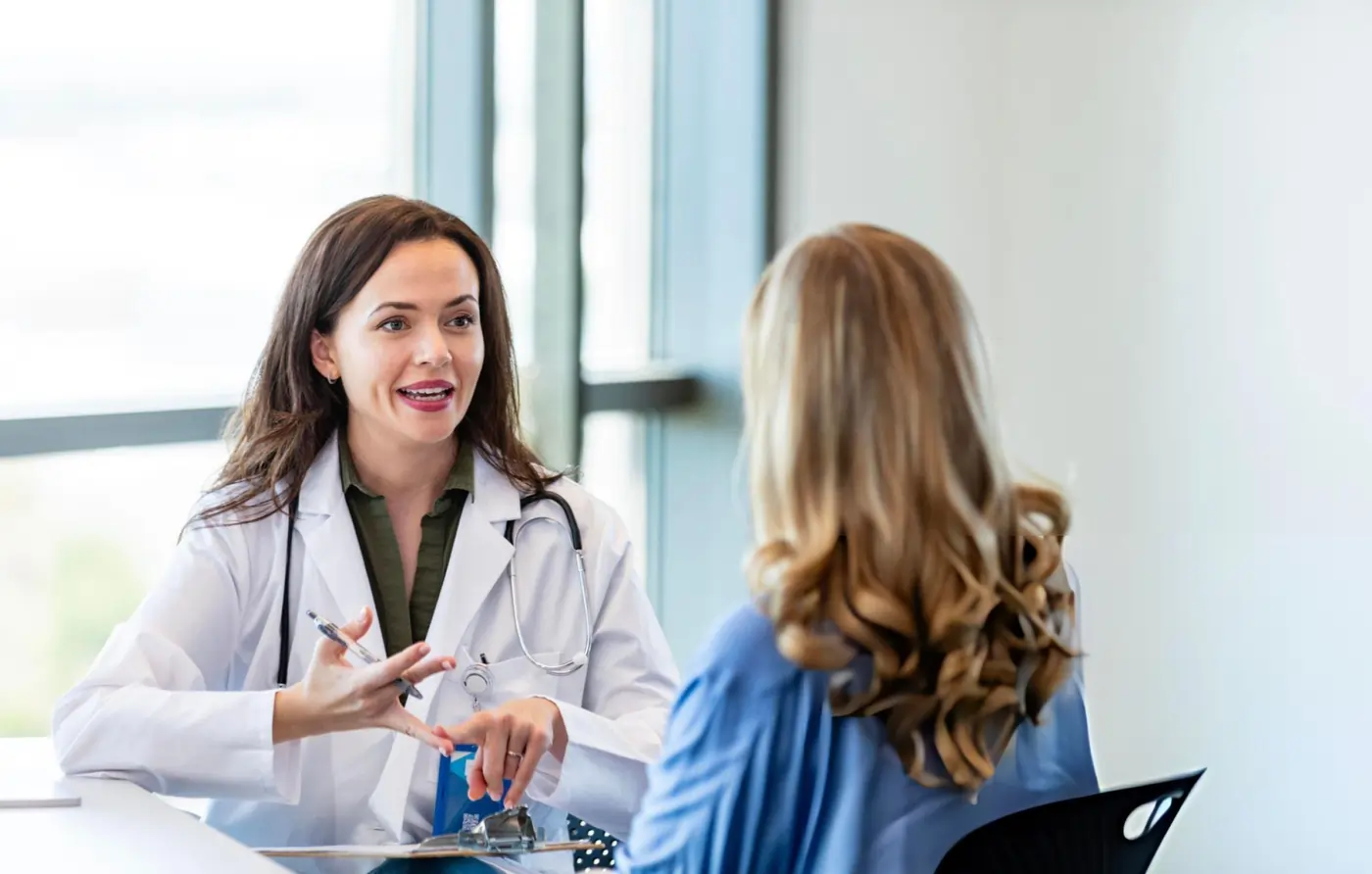 Female doctor in a white coat consulting with a patient in a bright medical office.