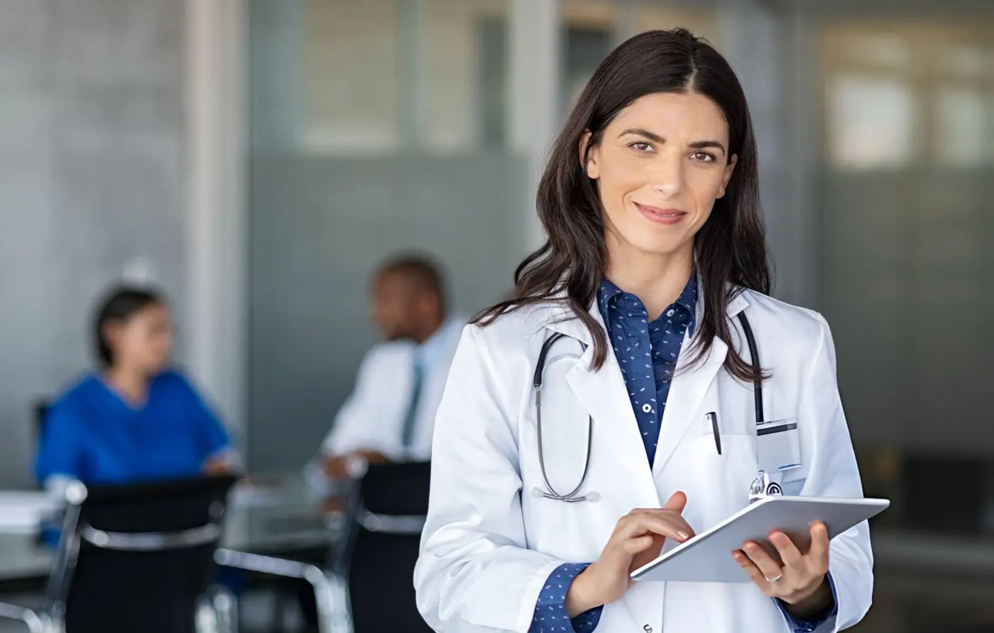 Female doctor in white coat holding a digital tablet in a medical office setting.