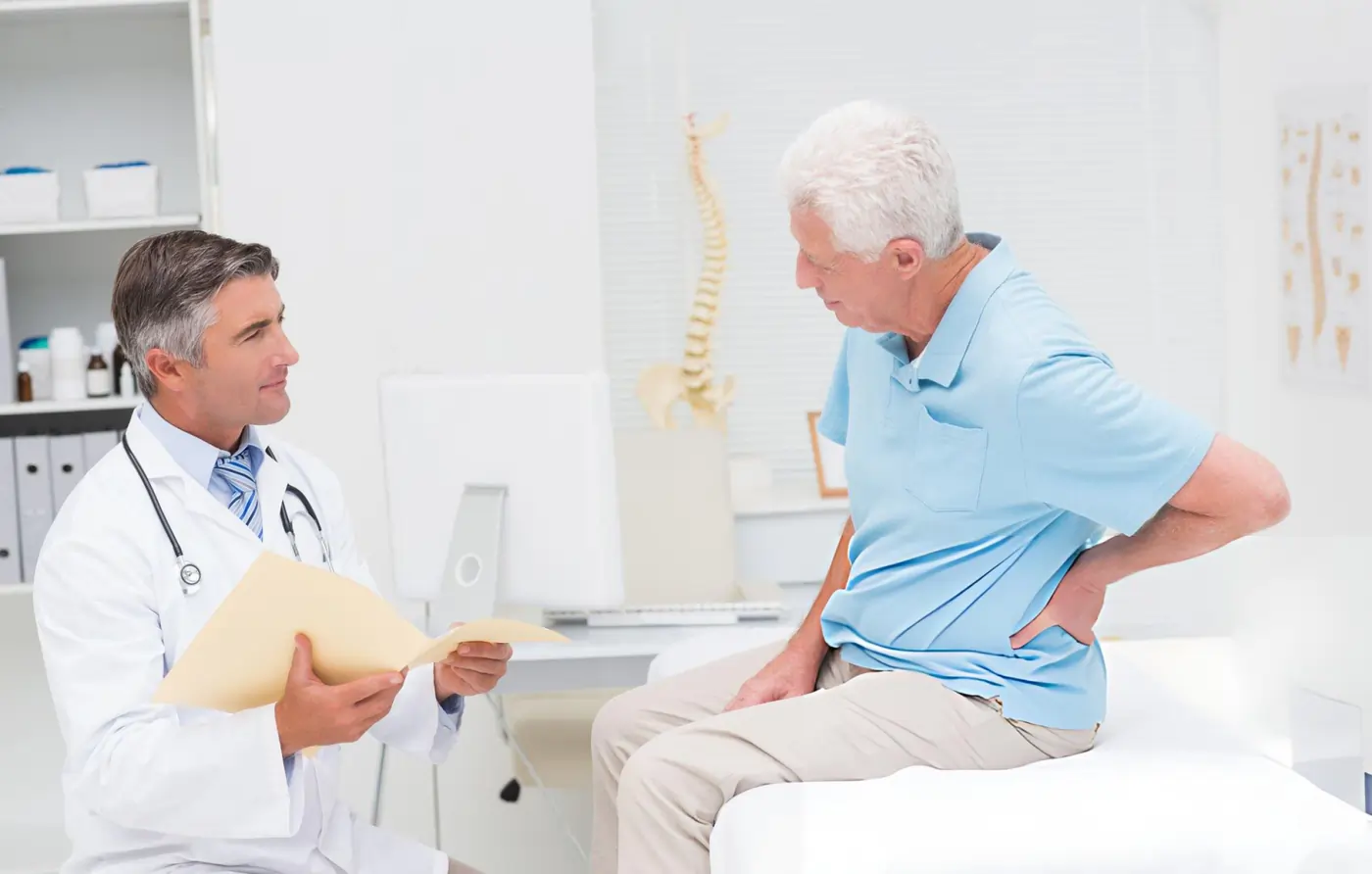 Doctor consulting senior man with lower back pain in medical office.