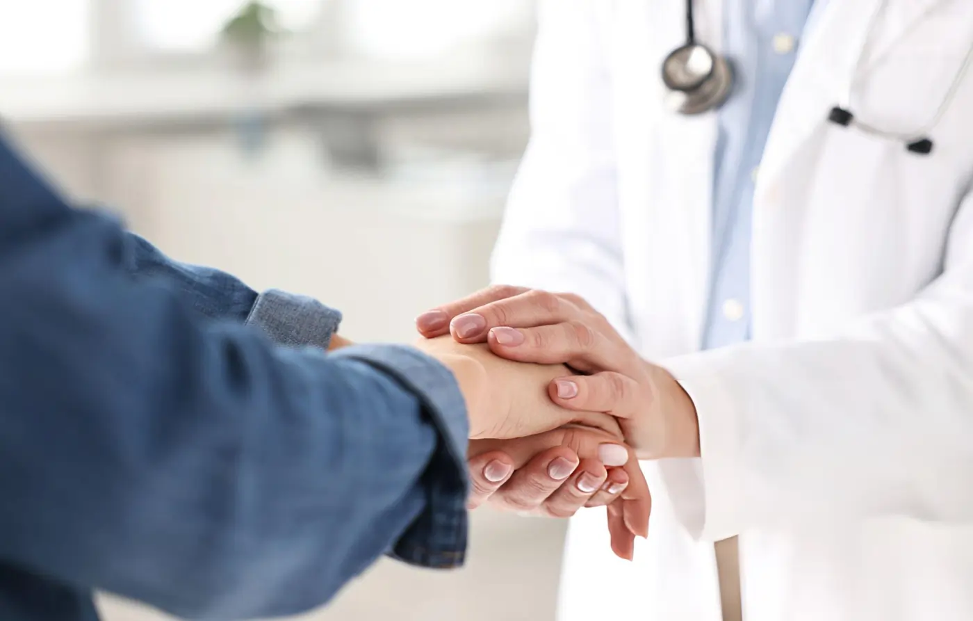Doctor holding patient's hand in support during medical consultation.