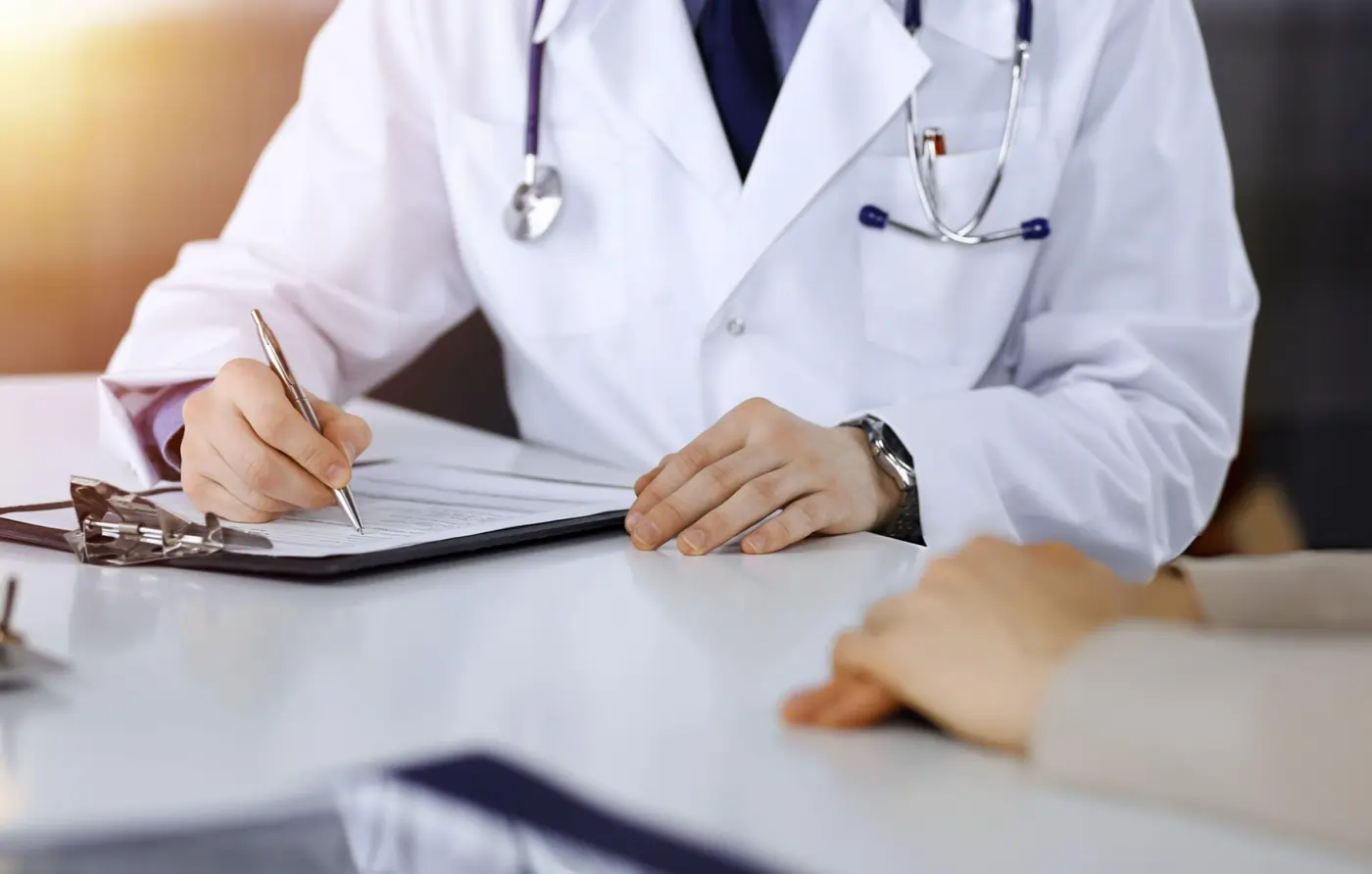 Doctor in white coat writing on medical clipboard during patient consultation.