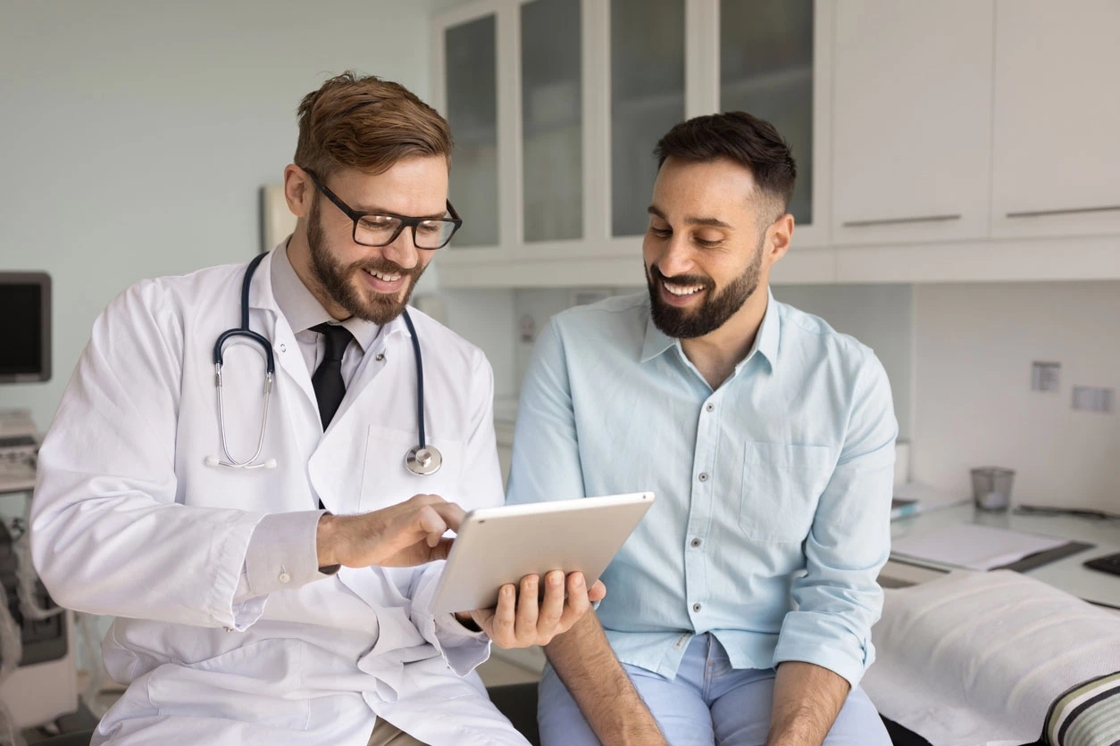 Positive male doctor and patient discussing medical examination results on a tablet in a Chattanooga clinic, providing regenerative medicine consultation based on medical records.