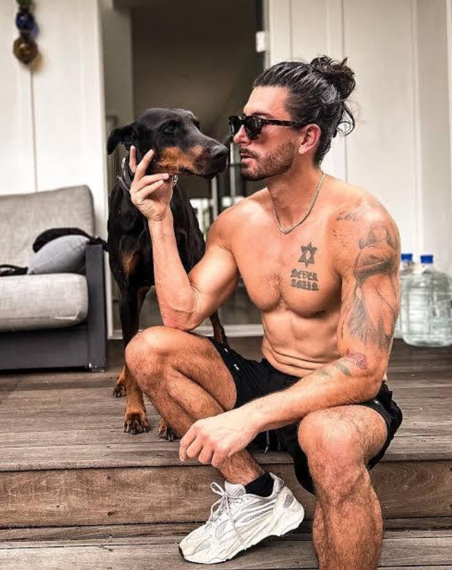 Jesse Wellens sitting shirtless on wooden steps with a Doberman dog, showcasing athletic physique and lifestyle as R3 Stem Cell brand ambassador