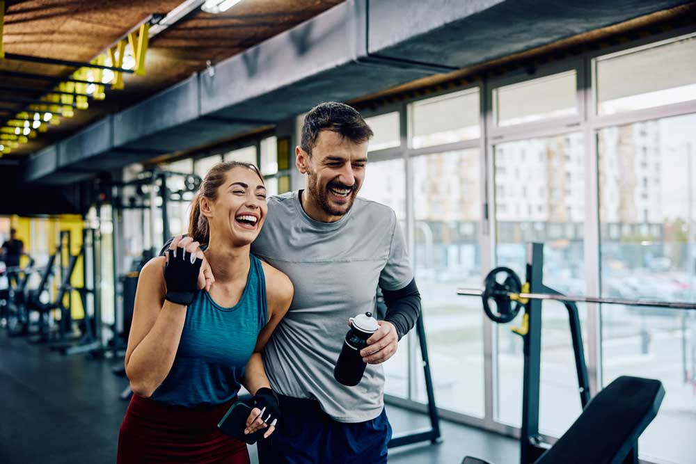 A happy, energetic couple laughing and walking together in a gym after a pain-free workout, representing the active lifestyle restored by regenerative therapy at R3 Las Vegas.