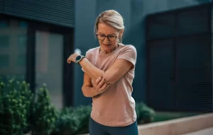 Active older woman holding her elbow in pain during outdoor exercise, representing joint pain in aging athletes that stem cell therapy can address