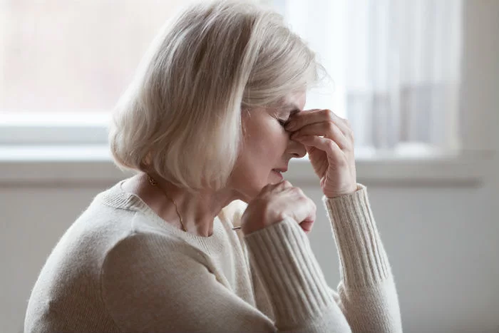 A senior woman holding her head in pain and exhaustion, representing patients with unique health concerns who can benefit from regenerative therapy at R3 Las Vegas.