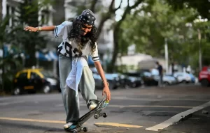 Young woman performing a skateboard trick on a city street wearing casual streetwear and a bandana.