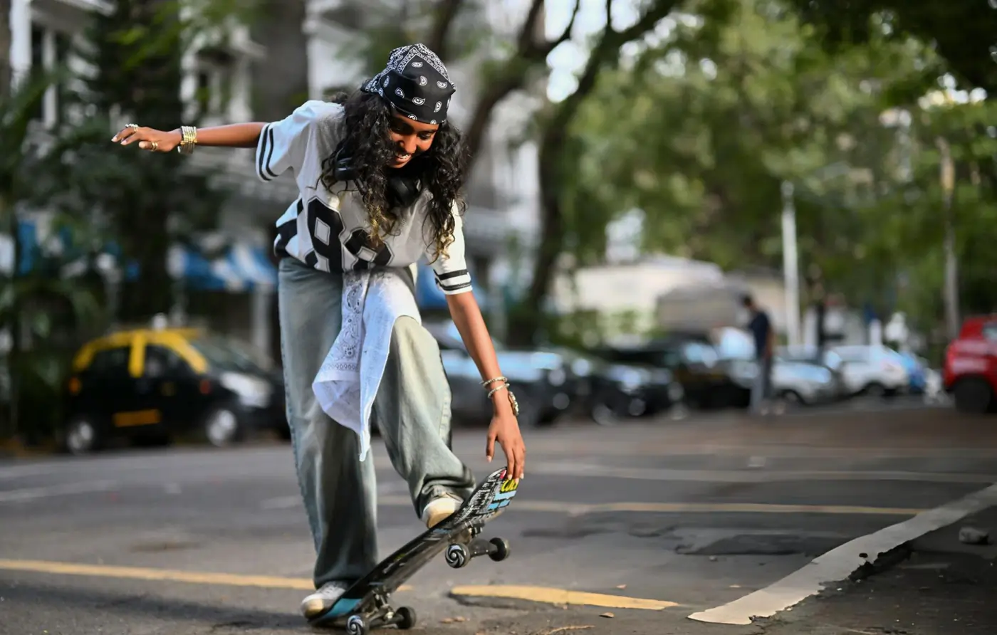 Young woman performing a skateboard trick on a city street wearing casual streetwear and a bandana.