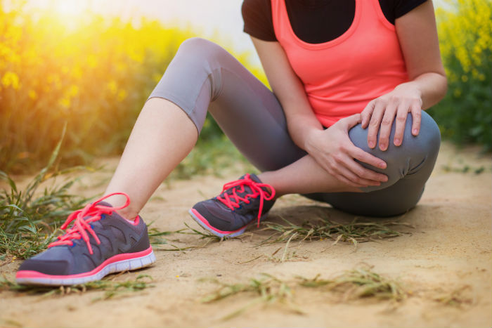 A woman holding her knee in pain while outdoors, seeking regenerative therapy in Irvine.