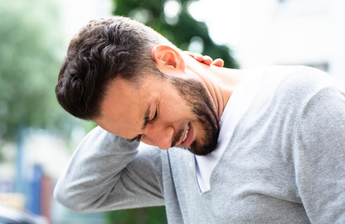 A young man holding his neck in severe pain and discomfort, representing chronic pain symptoms that can be successfully treated with regenerative therapy at R3 Long Beach.