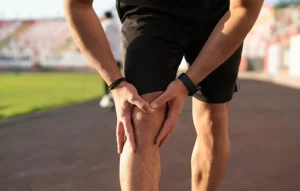 Athlete on a track holding his knee in pain, illustrating joint injuries treated with stem cell therapy.