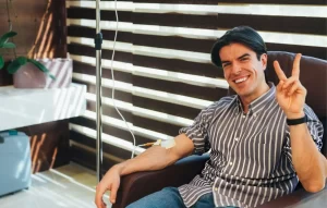 Patient receiving IV stem cell therapy infusion while seated comfortably in a clinic, smiling during regenerative medicine treatment for chronic health conditions.