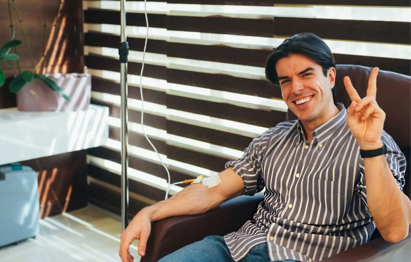 Patient receiving IV stem cell therapy infusion while seated comfortably in a clinic, smiling during regenerative medicine treatment for chronic health conditions.