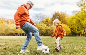 Active grandfather playing soccer with young grandchild in autumn park, representing restored mobility and quality of life after stem cell therapy for chronic back pain