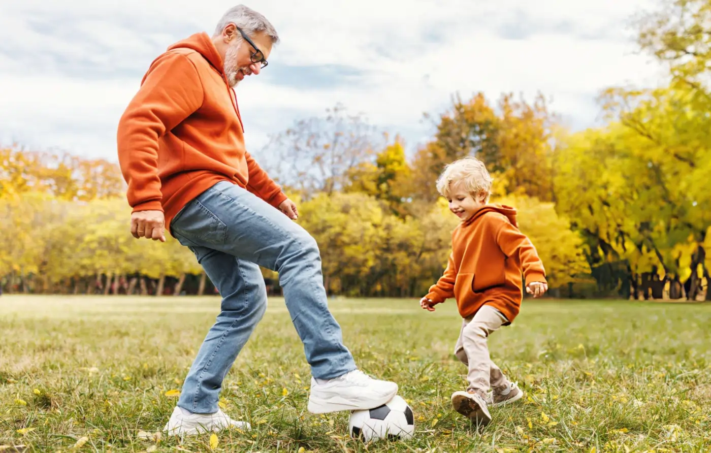 Active grandfather playing soccer with young grandchild in autumn park, representing restored mobility and quality of life after stem cell therapy for chronic back pain