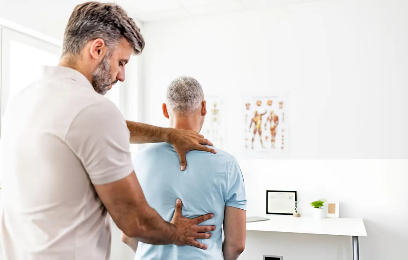 Physical therapist examining the upper and lower back posture of an older adult patient during a musculoskeletal assessment in a modern clinic.