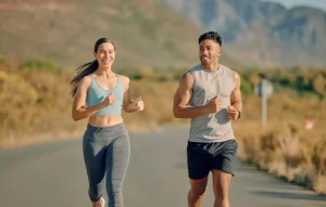 A fit young man and woman smiling and running together on an open outdoor road, representing healthy joint function and successful recovery from sports injuries or chronic pain.