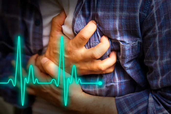 A man in a plaid shirt clutching his chest in pain with a bright cyan ECG heart rate line graphic overlaid, representing symptoms of heart failure and options for stem cell therapy in Mexico.