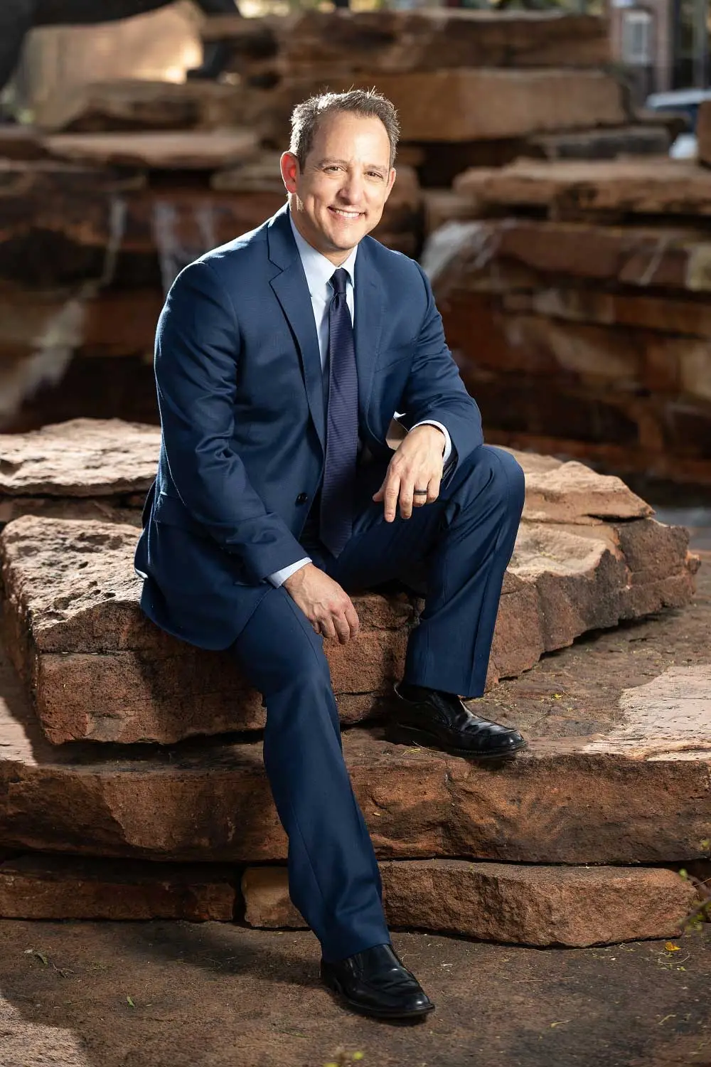 R3 Stem Cell founder in a blue suit smiling while sitting on stone steps.