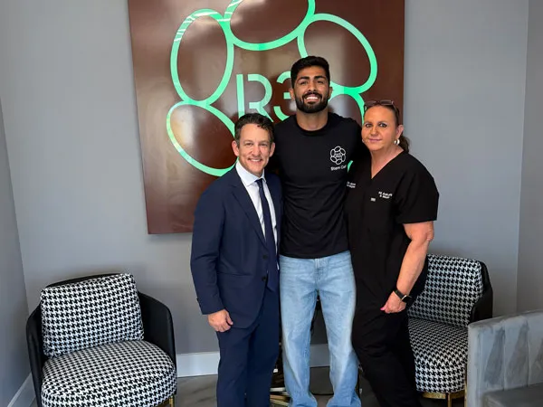 Dr. Greene, founder of R3 Stem Cell, with team members and patient in front of the illuminated R3 logo at our Orlando clinic